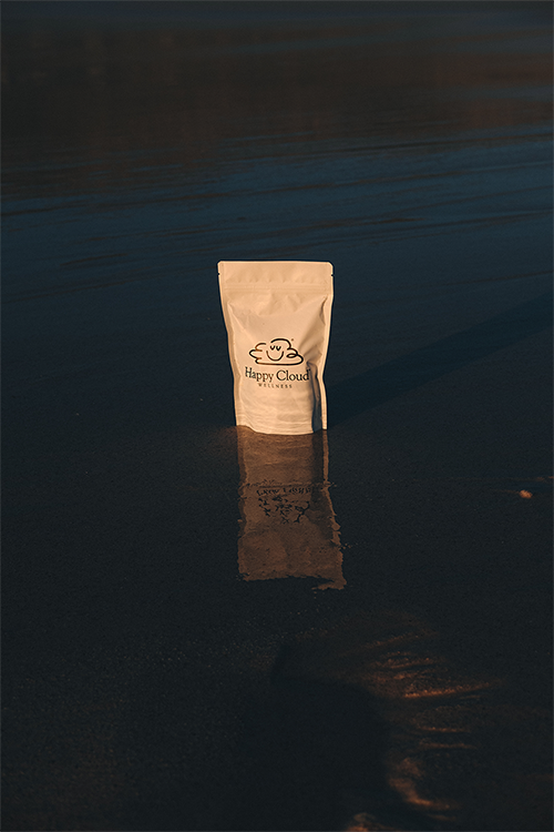 HCW A package labeled HC Chocolates Extra Strength stands upright on wet sand, reflecting on the surface, with calm water and a dark, serene background. Happy Cloud Wellness